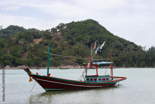 Colorful traditional Thai fishing boat floating near tropical island coast. Seascape with fishing vessel and green hills, Koh Phangan island, Thailand.