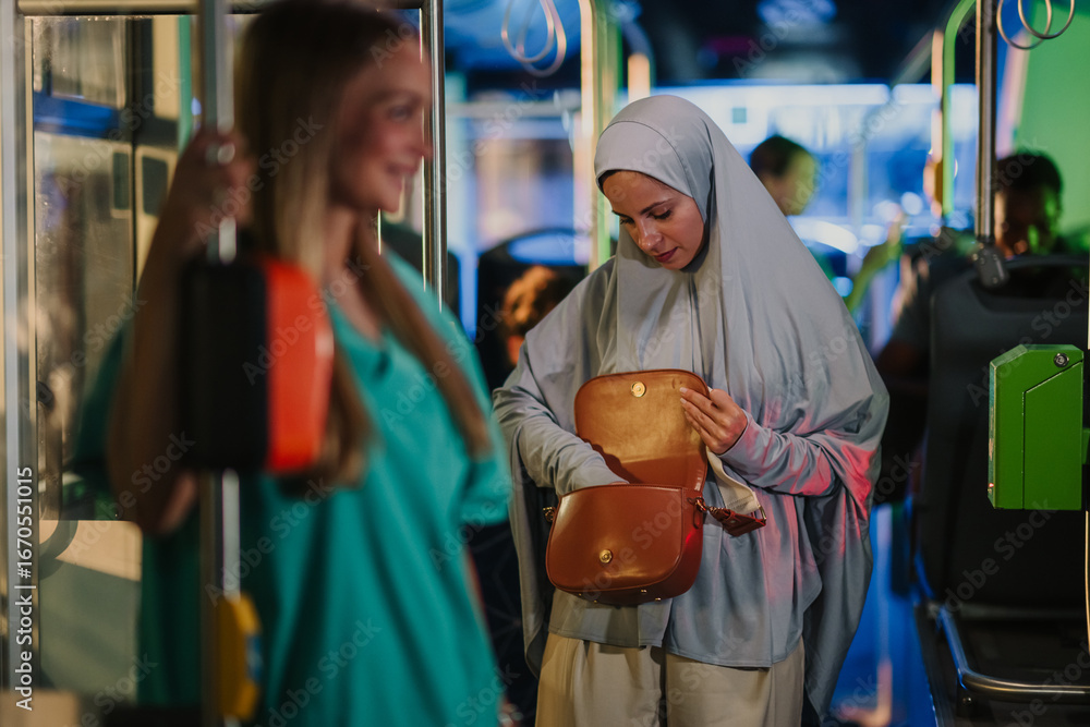 Fototapeta premium Muslim woman searching in her bag on a public transport bus