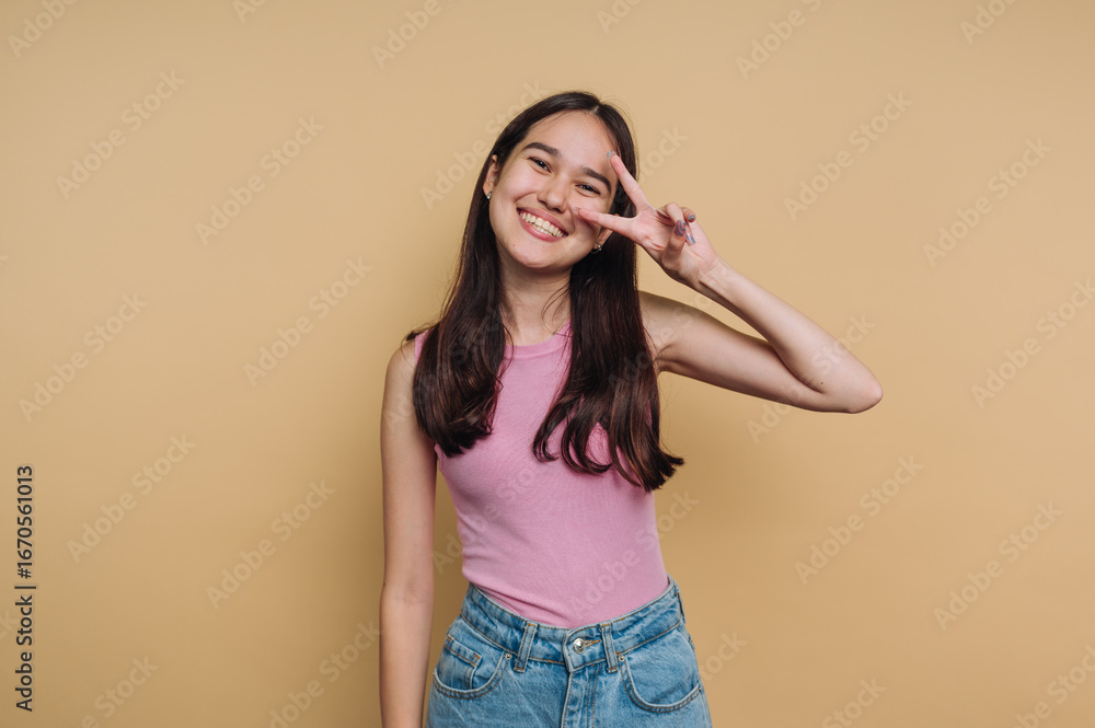 Fototapeta premium Young girl smiling and posing playfully against a yellow background in a casual outfit during a bright afternoon