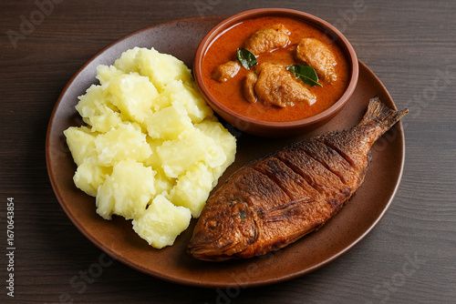 Boiled and mashed tapioca served with spicy chicken curry and crispy fried fish stock photo