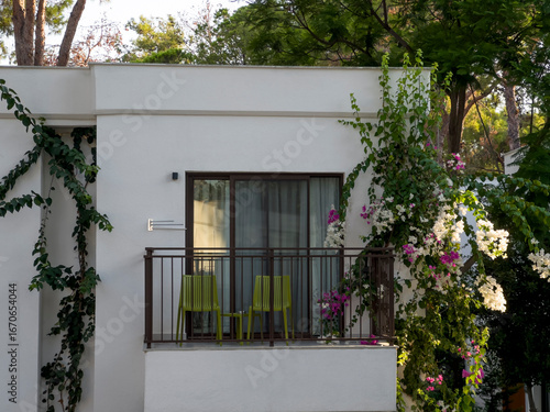 Balcony with green plastic chairs against a white building facade. 