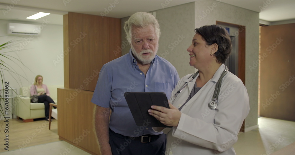 Obraz premium Senior man reviewing health information with female doctor in clinic hallway, holding digital tablet during calm and professional healthcare consultation