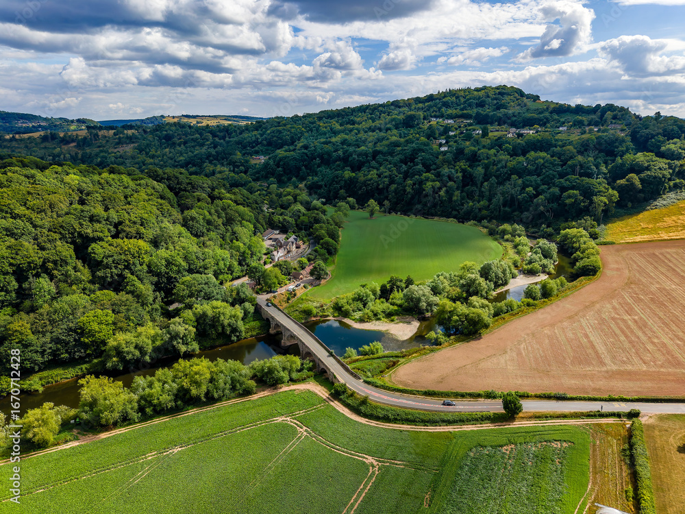 Fototapeta premium Scenic English countryside with a historic bridge over a winding river in summer.