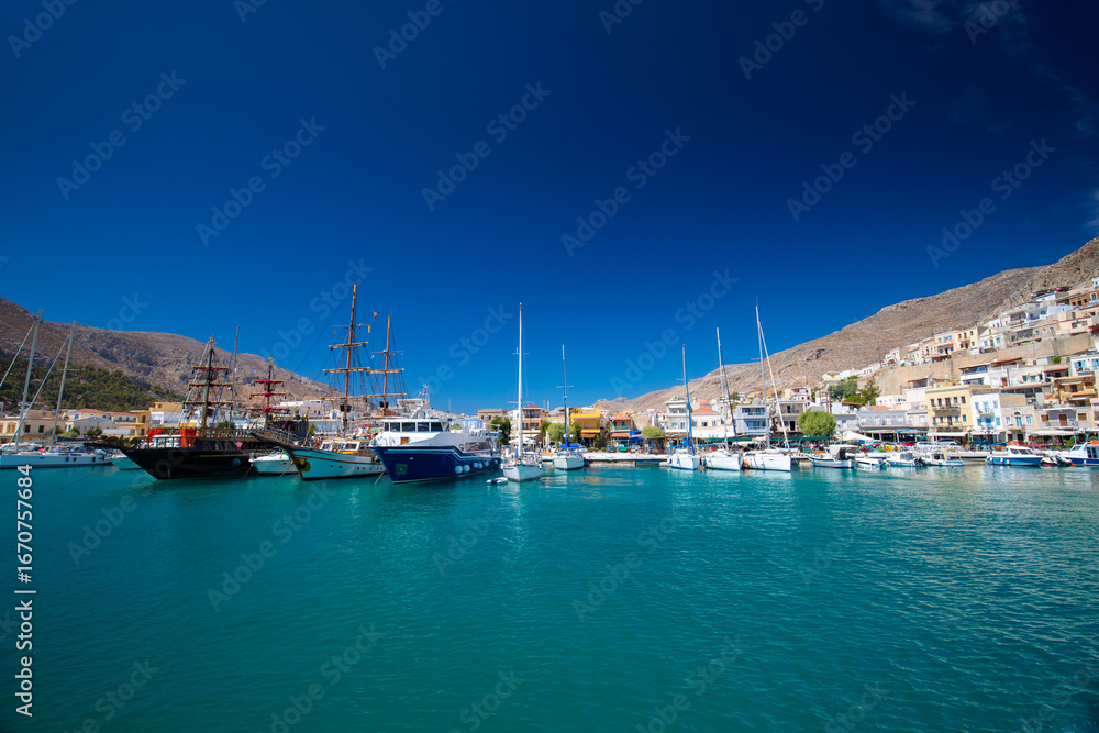 Obraz premium Scena portu z łodziami i budynkami pod czystym, niebieskim niebem, Kalymnos, Grecja , tło lub tapeta do projektu