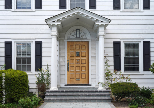 Traditional two story white clapboard house with wood grain front door
