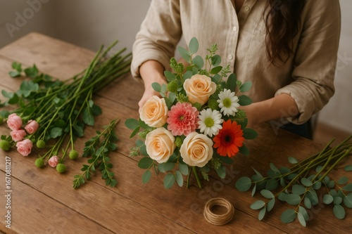 Florist skillfully arranging a vibrant bouquet filled with roses, dahlias, and eucalyptus leaves on a rustic wooden table