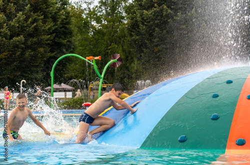 Children climbing and sliding on large inflatable water dome structure with colorful climbing holds at public splash parke. Active water play, physical fitness and outdoor fun. High quality photo