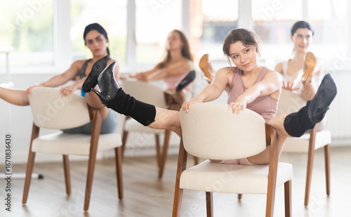 Girls in high heels and shorts sit on chair and performs combination of lap dance movements in group lesson. Training to perform striptease for visitors, allurement clients with sexy female body