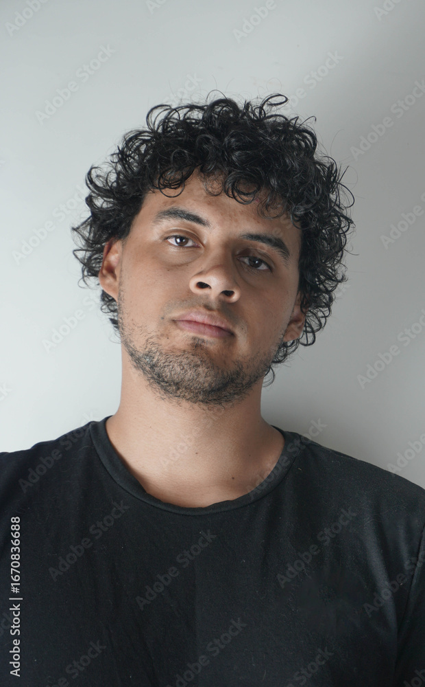 Obraz premium Latino boy with curly hair on a white background and a black t-shirt