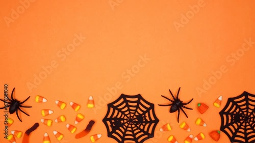 Halloween bottom border of scattered candy and spider webs. Top view stop motion loop video over an orange background with copy space.