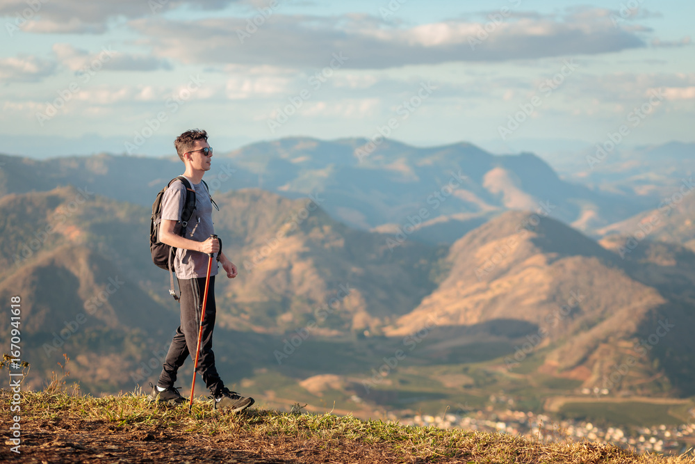 Fototapeta premium Brazilian man hiking with trekking pole on a sunny day, enjoying the mountain landscape during a seasonal outdoor adventure.