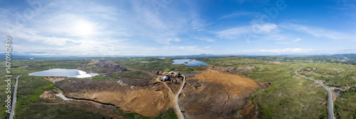 Expansive Aerial Panoramic view captures the remnants of a closed copper mine in Røros, Norway, highlighting the desolate terrain and reflecting sunlight under a blue sky