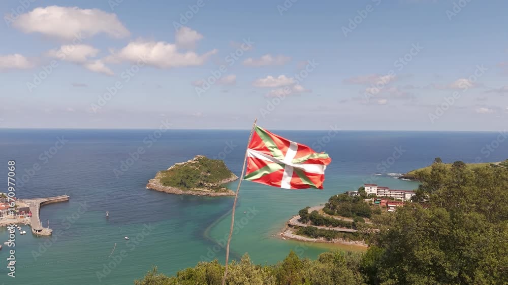 Basque flag waving over the coastline of Lekeitio with San Nicolas island and blue sea views