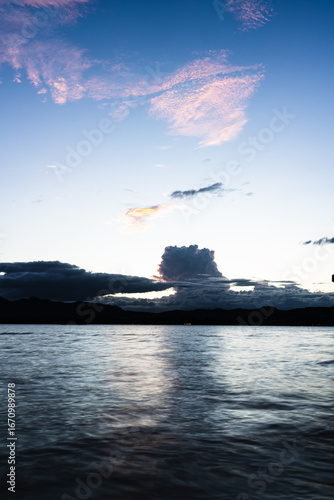 A serene twilight scene over a calm lake with distant hills and a glowing hor...