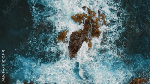 Aerial of churning sea waters embrace weathered rocks on a bold coastal platform