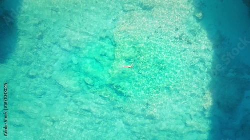 Top down view of woman floats alone in crystal clear turquoise water with sunlit ripples