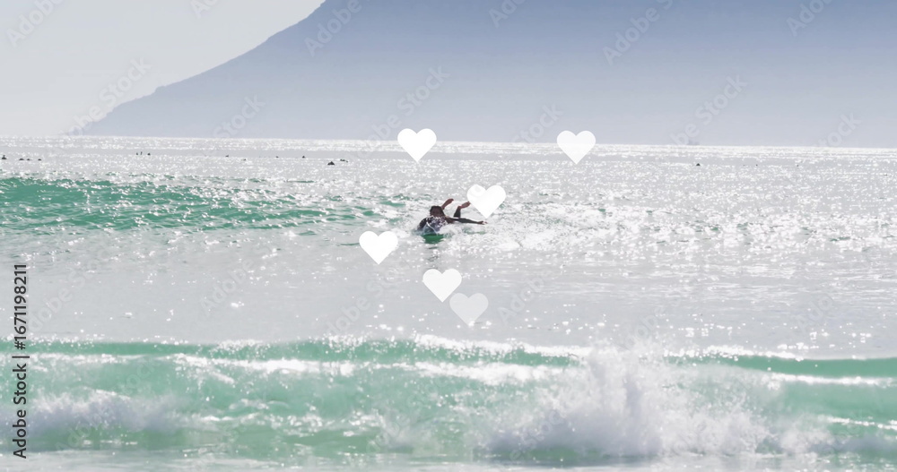 Obraz premium Gliding female surfer paddling on surfboard in ocean surf zone, with wetsuit and sparkling waves