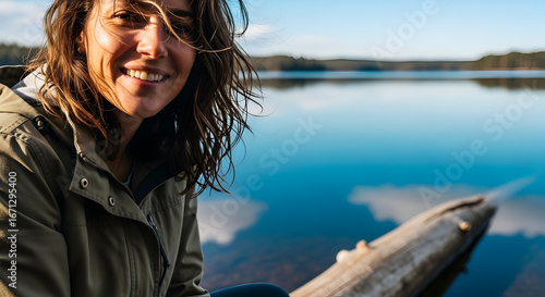 Happy woman enjoying outdoor fishing by calm lake with scenic landscape and clear blue sky in the background for outdoor recreation and leisure activities