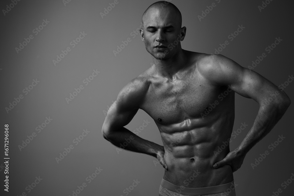 Fototapeta premium Black and white image of a muscular man posing confidently, showcasing his toned physique and athleticism, exuding strength and determination.