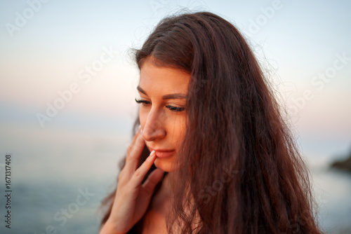 Tableau sur toile Sunset lit woman with flowing brown hair gently caressing cheek while gazing dow
