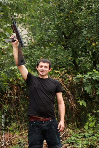 A criminal in black shirt with submachine gun in hands standing in the park