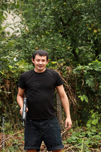 A criminal in black shirt with submachine gun in hands standing in the park
