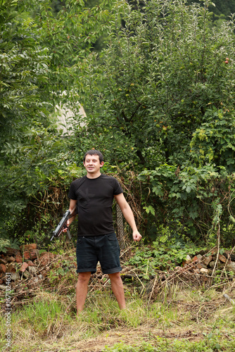 A criminal in black shirt with submachine gun in hands standing in the park