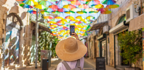 Back view of female traveler taking pictures of landmarks on her phone in the historic city of umbrella sky.