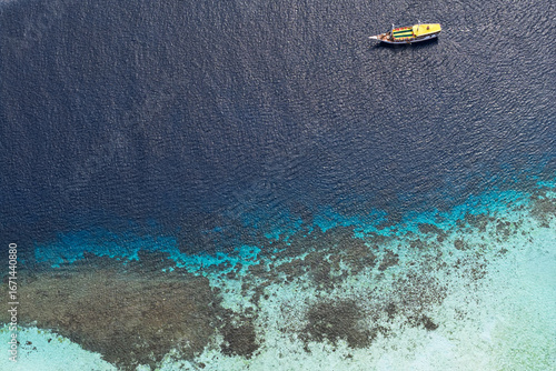 Aerial view of a boat drifting on the tranquil turquoise and deep blue waters near the coral reef, Pink Beach, East Nusa Tenggara, Indonesia.