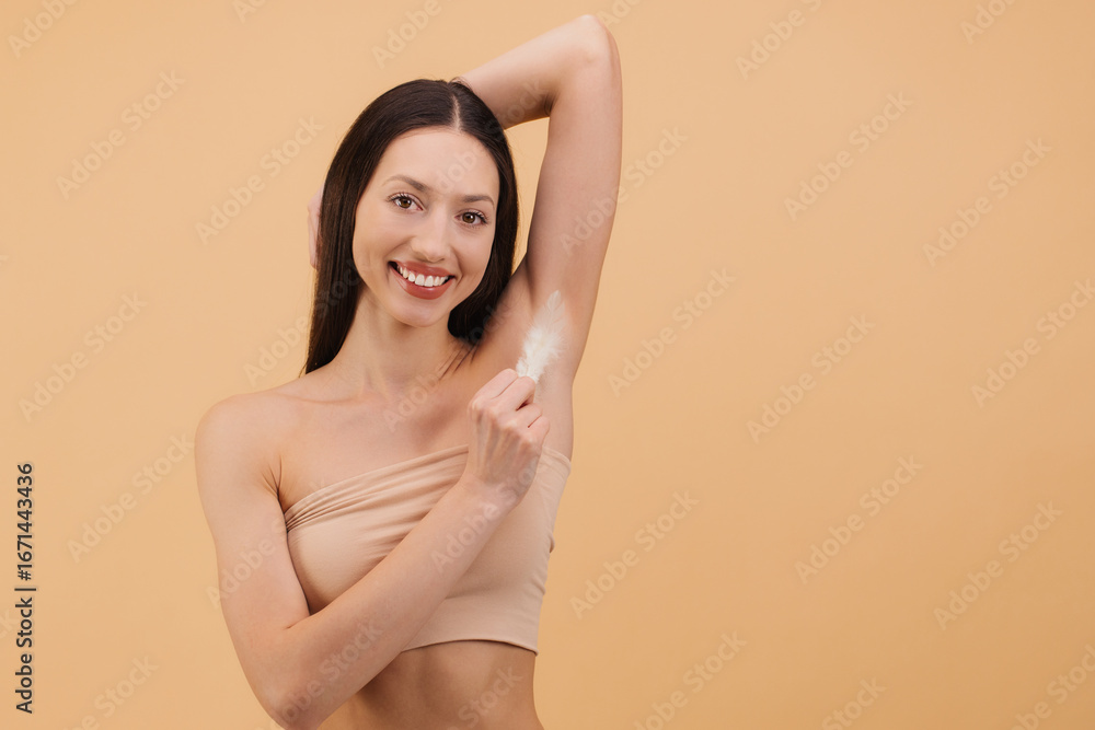 Obraz premium Smiling woman applying deodorant cream on her armpit on beige background