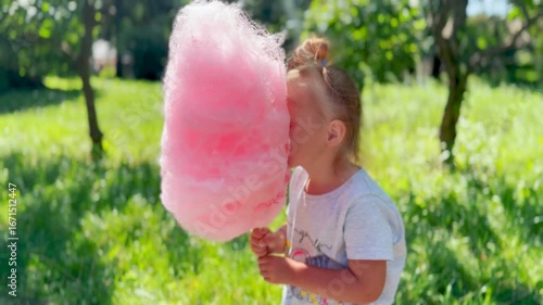 Little girl enjoying pink cotton candy outdoors. A symbol of sweet treats and summer celebration