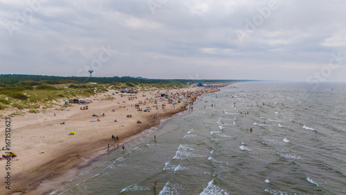Fototapeta Naklejka Na Ścianę i Meble -  Šventoji beach on the Baltic Sea in Lithuania, with sandy shore, rolling waves, dunes, and holidaymakers enjoying summer relaxation by the coastline