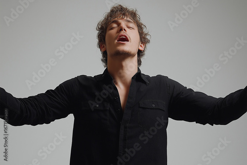 Expressive young man in black shirt raising arms, emotional gesture of hope, drama and passion, studio portrait of actor performing, artistic male expression, theatrical body language concept