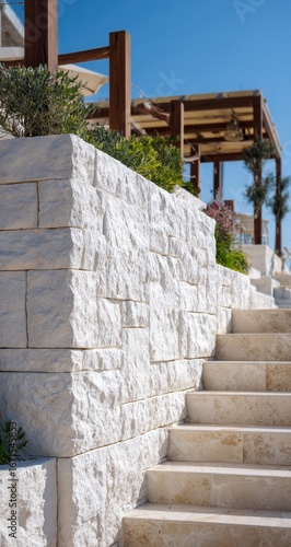 White stone retaining wall with steps leading up to a pergola
