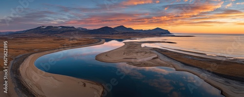 A breathtaking aerial view of a winding river meeting the ocean at sunrise, showcasing the beautiful interplay of water, sand, and mountains.