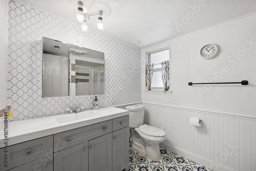 A bathroom featuring a sink, toilet, mirror, and a clock on the wall