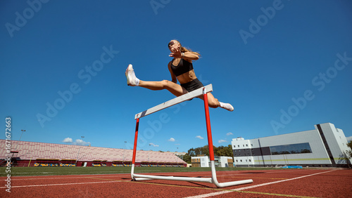 Female hurdler powerful leap above hurdle against clear sky. Concept of freedom, empowerment, sport challenge, mental resilience, and professional athletic success.