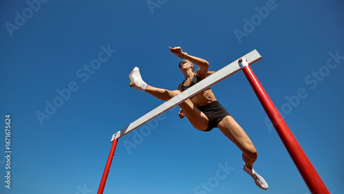Foto Female hurdler in low angle action leap against clear sky