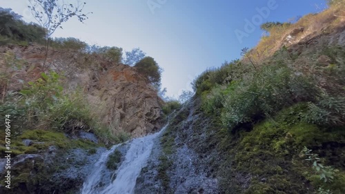 Upward view along a small mountain waterfall flowing between rocks. Scenic natural landscape with fresh water, rugged cliffs, and wilderness atmosphere showing beauty of untouched highland nature and 