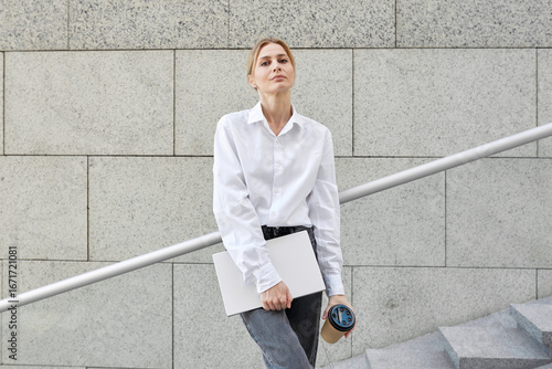Confident blond young business woman going to a meeting with a cup of coffee and laptop