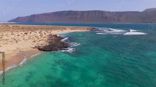Aerial Drone Shot Flying Over La Graciosa Island And Atlantic Ocean With Distant Lanzarote, Canary Islands, Spain On A Bright Day.