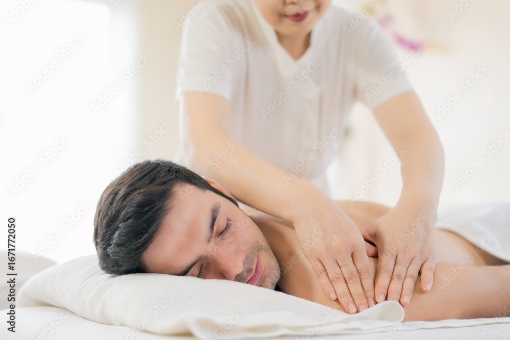 A man receiving a relaxing back massage at a spa, lying face down on a massage bed with a white towel. The therapist is applying gentle pressure on his shoulder muscles, a peaceful and atmosphere. A man receiving a relaxing back massage at a spa, lying face down on a massage bed with a white towel. The therapist is applying gentle pressure on his shoulder muscles, a peaceful and atmosphere.