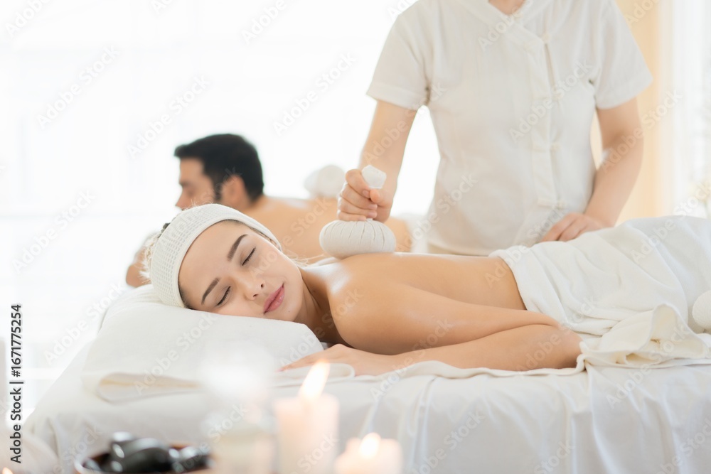 Obraz premium Couple receiving herbal compress massage in spa. A trending holistic therapy for stress relief, wellness, and self-investment.