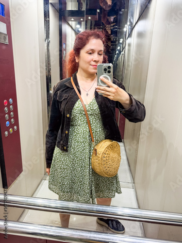 Woman taking mirror selfie in elevator with smartphone. Everyday lifestyle, modern technology, and urban routine in personal perspective.