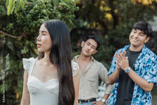 Foto A composed young Asian woman looks away in silence as two smug young men behind her make inappropriate comments and catcall her outdoors