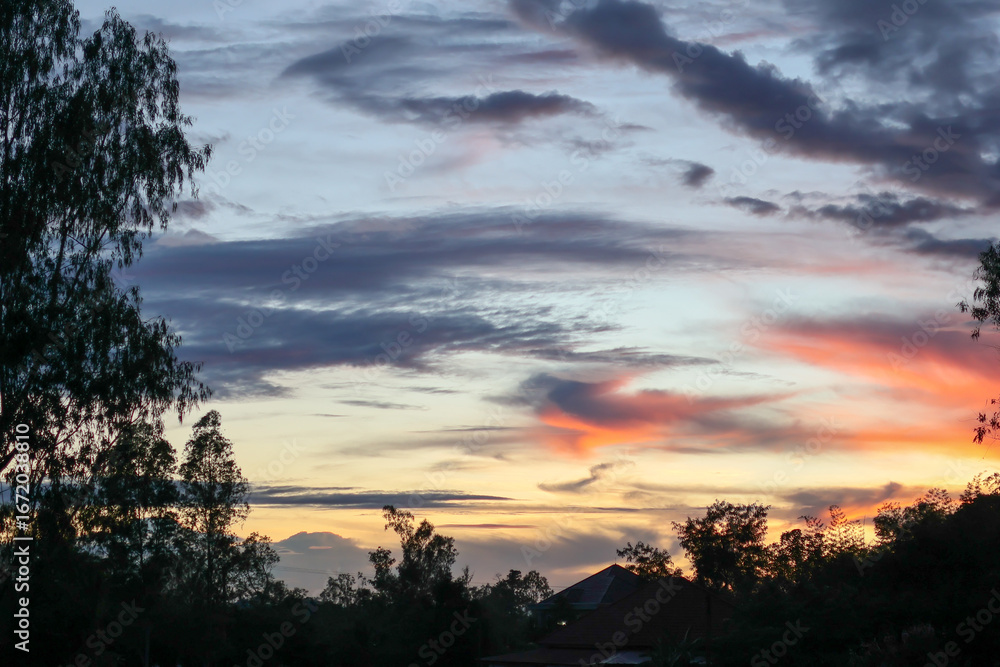 Obraz premium A breathtaking time lapse captures the sun's descent, casting a dramatic orange glow across storm clouds as they gather over the tree landscape