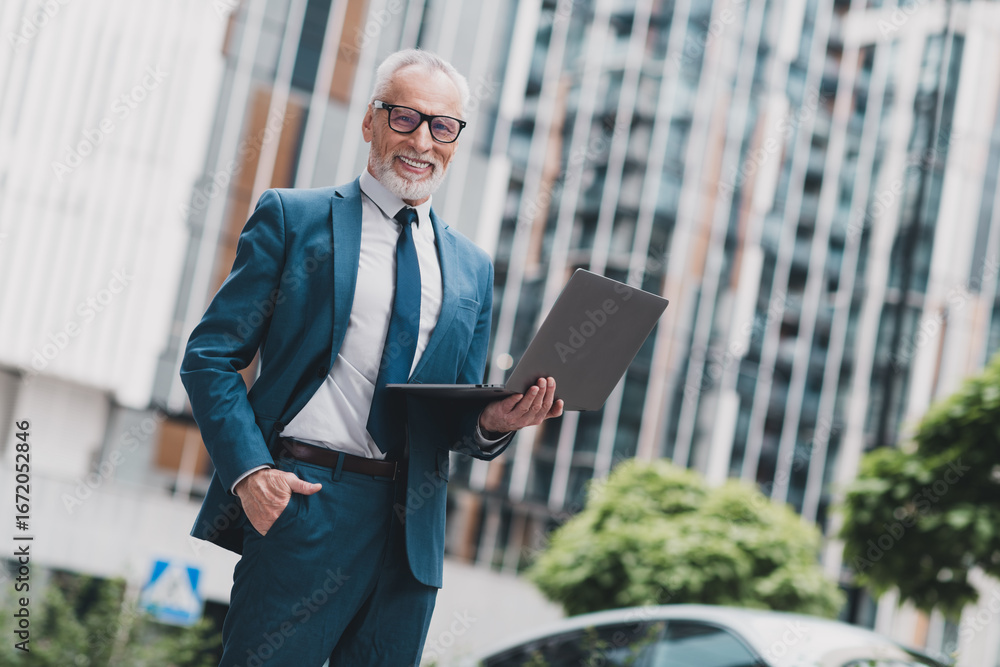 Fototapeta premium Successful mature businessman holding laptop outdoors in urban setting demonstrating success in real estate management