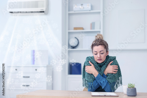 Broken air conditioner or temperature set too low. Woman with scarf freezing at workplace in office