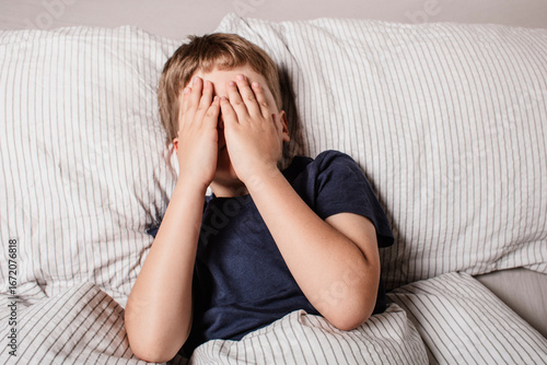 The child was scared before going to bed. Night terrors in a child. The kid covers his face with his hands in a fear. Children's experiences. Sad psychological state. Nightmares or fear of darkness.