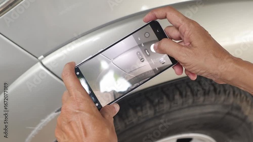 Female car insurance officer's hand uses smartphone take photo scratched wheel arch and damage from collision with concrete wall as evidence for a car insurance claim at a service center.